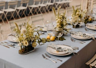 A wedding table setting with blue grey tablecloths and patterned napkins, fluted glassware and fresh lemons