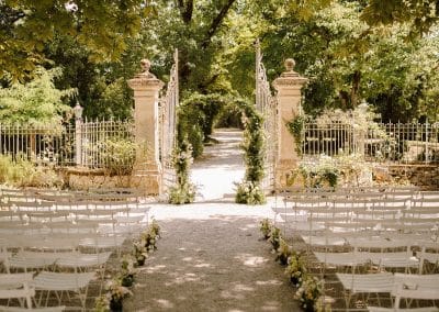 The courtyard at Chateau de Lartigolle set up for a wedding ceremony. Rows of chairs for guests under the sahed of the chestnut trees. The wedding arch constructed over the chateau gates.