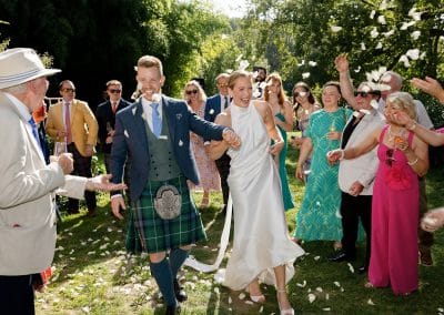 Bride and Groom hold hands and are welcomed to the drinks reception with confetti
